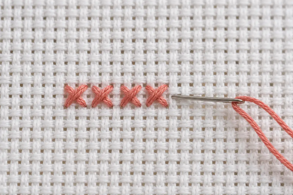 Close view of a neat row of coral cross stitches with a tapestry needle